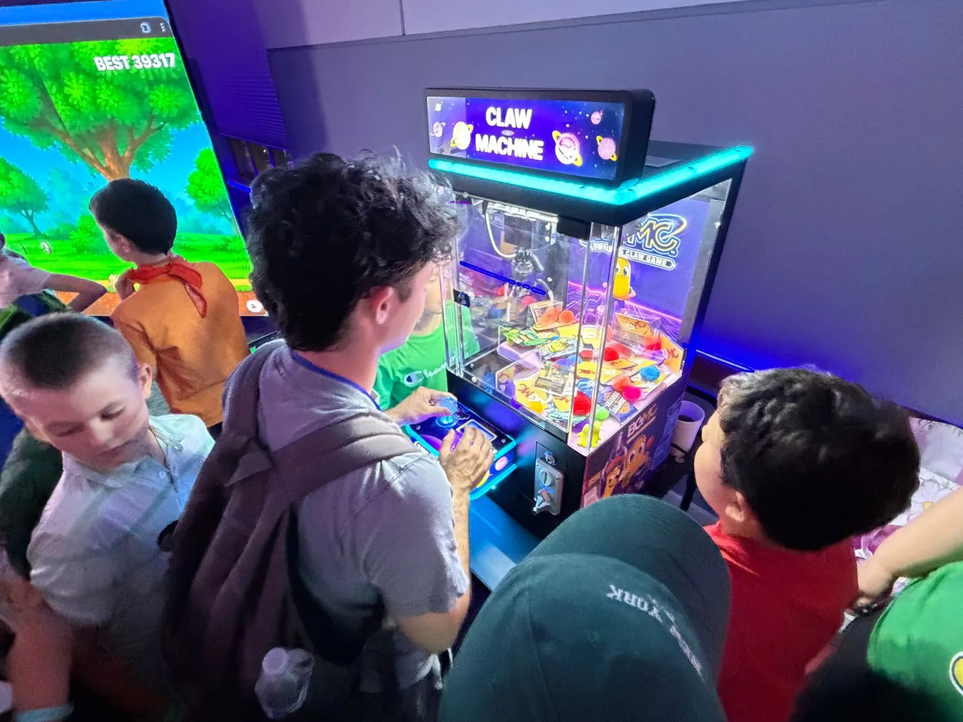 Children try the illuminated BGMC claw machine filled with cards and prizes.